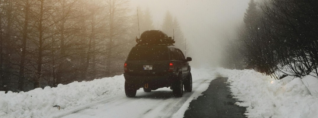 A stock photo of an SUV driving down a winter road.